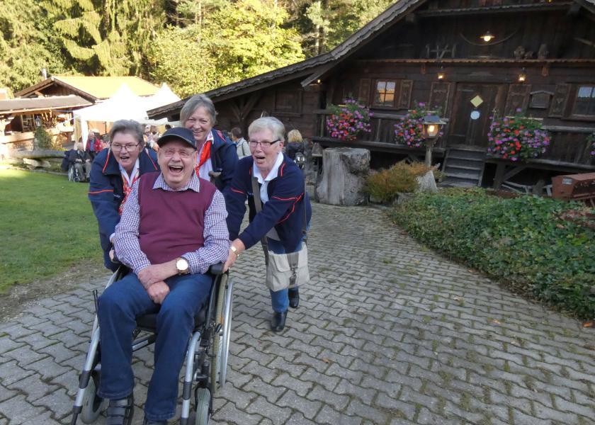 Älterer Mann im Rollstuhl wird durch drei Frauen Berg hochgeschoben