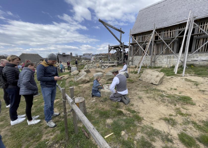 Besucher stehen vor einer Baustelle, bei der ein altes Haus renoviert wird, ein traditioneller Handwerker erklärt einem Kind die traditionelle Handwerkstechniken