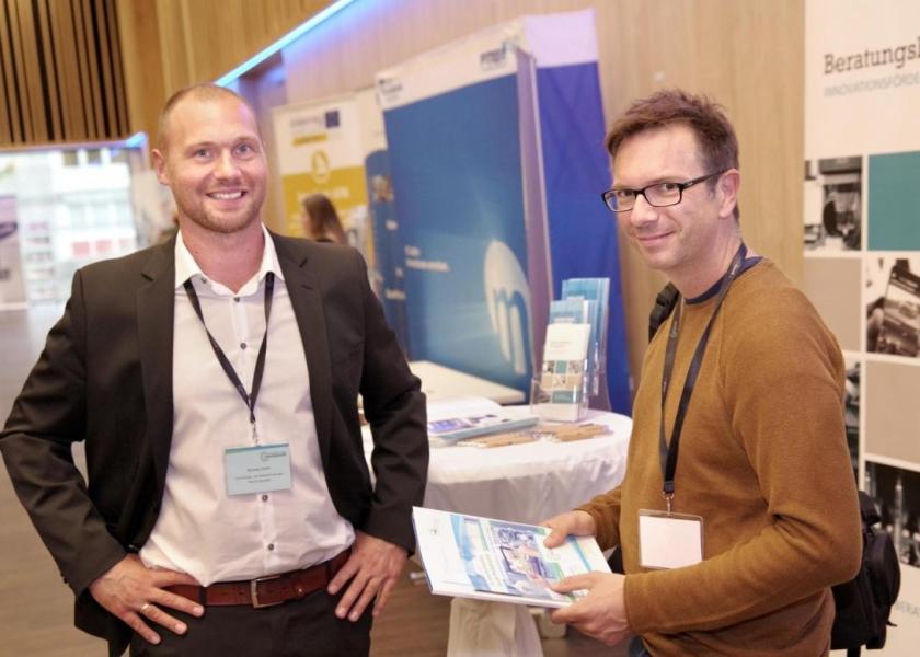 Zwei Männer vor einem Messestand des Beratungsbüros