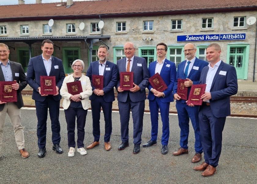 8 Personen stehen an einem tschechischen Bahnhof und halten eine repräsentative Mappe in der Hand