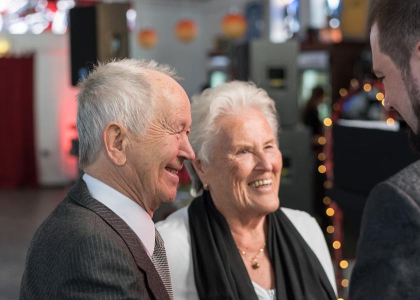 Ein Senior und eine Seniorin (gut angezogen) lachen einen Mann an