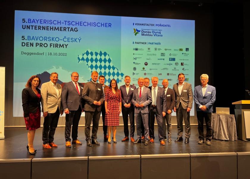 Menschen stehen auf einer Bühne, im Hintergrund: Leinwand mit 5. Bayerisch-Tschechischer Unternehmertag