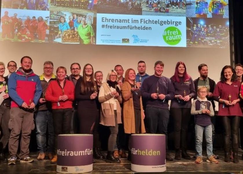 Gewürdigte Personen stehen auf der Bühne, im Hintergrund Präsentation Ehrenamt im Fichtelgebirge #freiraumfürhelden