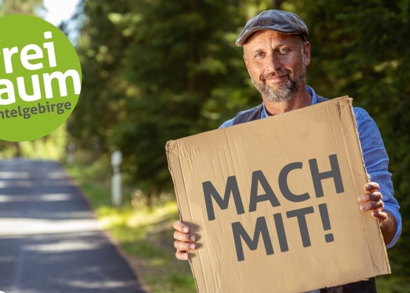 Mann hält Schild hoch mit Schriftzug MACH MIT!, links daneben Logo #freiraum fichtelgebirge