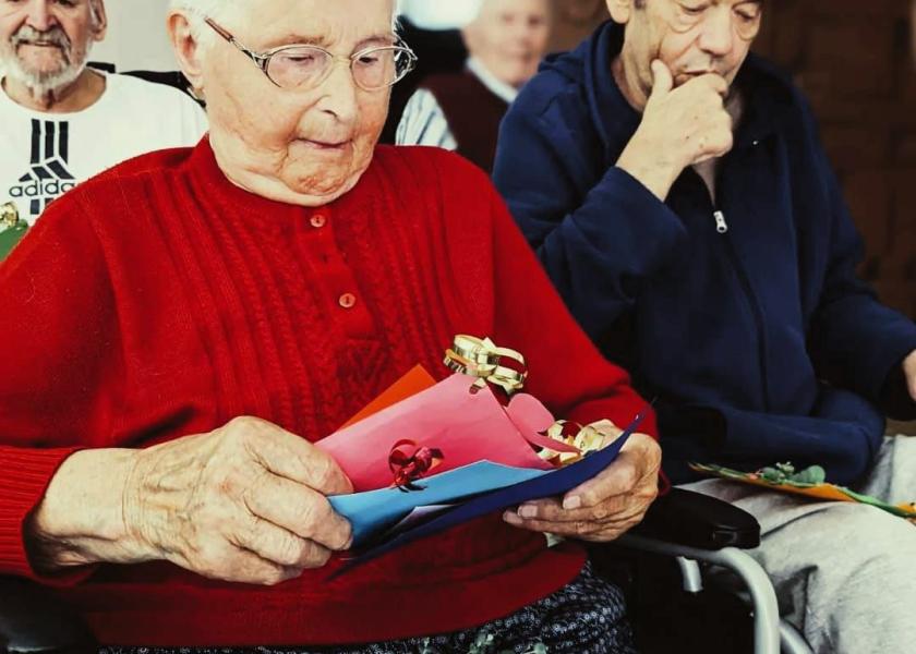 Zwei Senioren, die beide im Rollstuhl sitzen, lesen selbst gebastelte Karten 