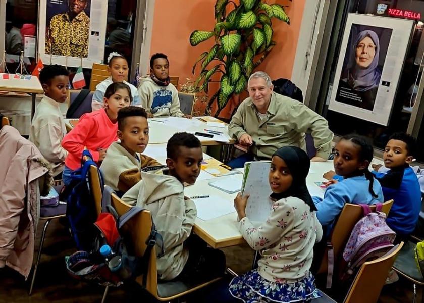 Älterer Mann und Kinder mit Migrationshintergrund sitzen rings um einen Tisch
