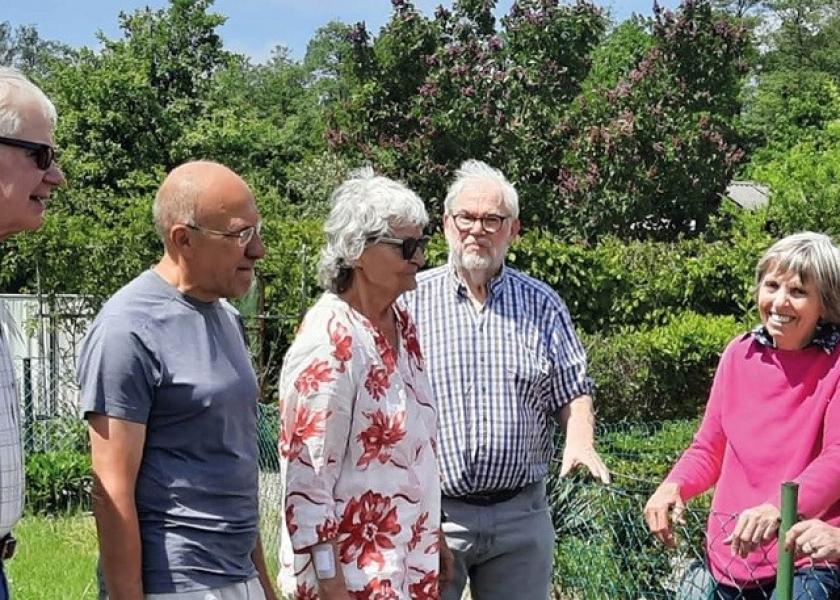 7 Personen stehen beieinander und unterhalten sich über Gartenzaun