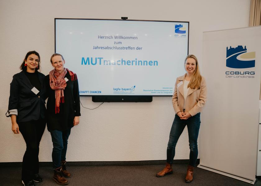 Drei Frauen stehen vor großem Bildschirm