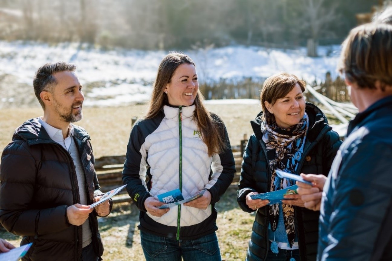 ein Mann und zwei Frauen stehen in der Natur (im Hintergrund ist Schnee sichtbar) und halten die OBERLANDCard in der Hand, auf der rechten Seite steht ein Mann mit dem Rücken zur Kamera mit Karte