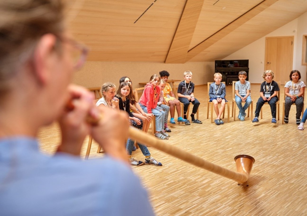 Mann spielt Didgeridoo und Kinder sehen zu 