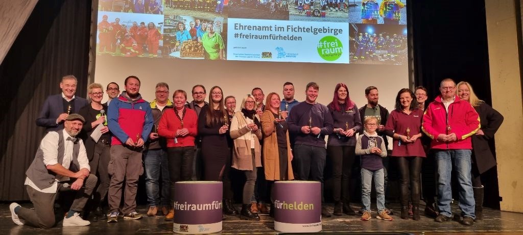 Gewürdigte Personen stehen auf der Bühne, im Hintergrund Präsentation Ehrenamt im Fichtelgebirge #freiraumfürhelden