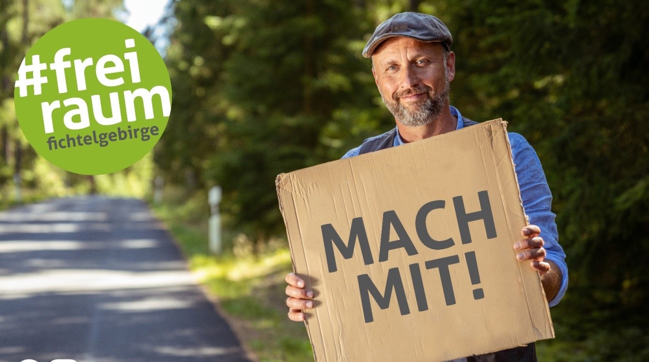 Mann hält Schild hoch mit Schriftzug MACH MIT!, links daneben Logo #freiraum fichtelgebirge